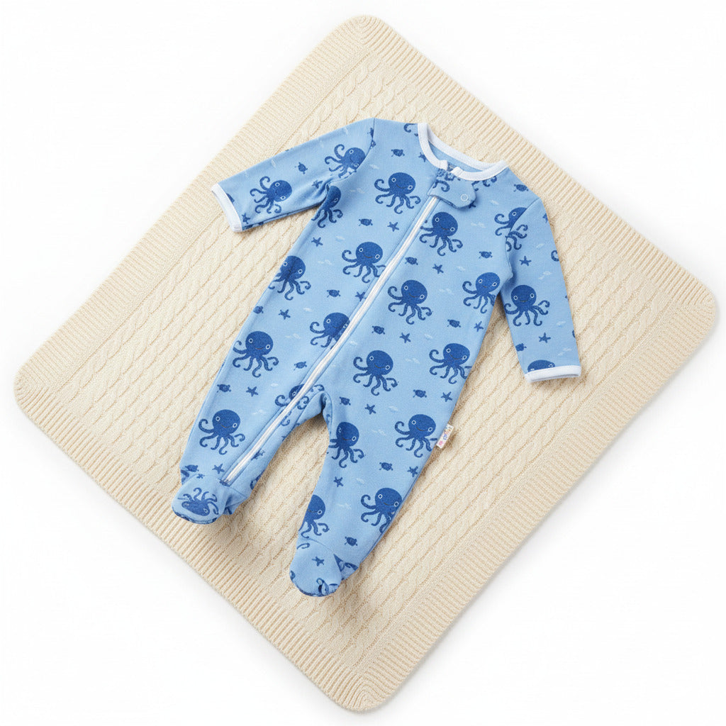 Three baby long-sleeve footless one-piece sleepers shown side by side on a white background: a white sleeper with pink flamingo print, a red sleeper with blue trim and a blue octopus graphic, and a blue sleeper with a subtle blue pattern.