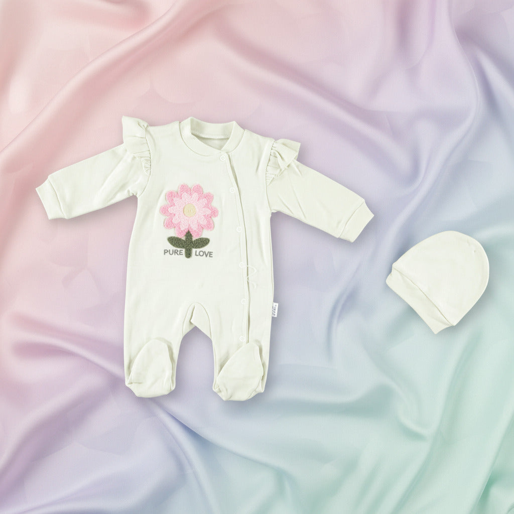 An off-white long-sleeve baby footed sleeper with ruffled shoulders and a pink flower graphic on the chest, shown next to a matching off-white bonnet on a white background.