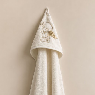 A white hooded towel with embroidered detailing on the hood, hanging against a light beige wall.