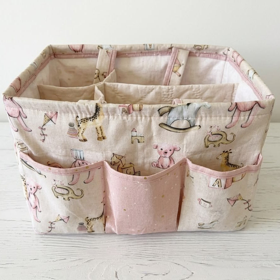 A fabric storage organizer basket with multiple compartments and front pockets, featuring a pink and beige animal print on a white wooden surface.