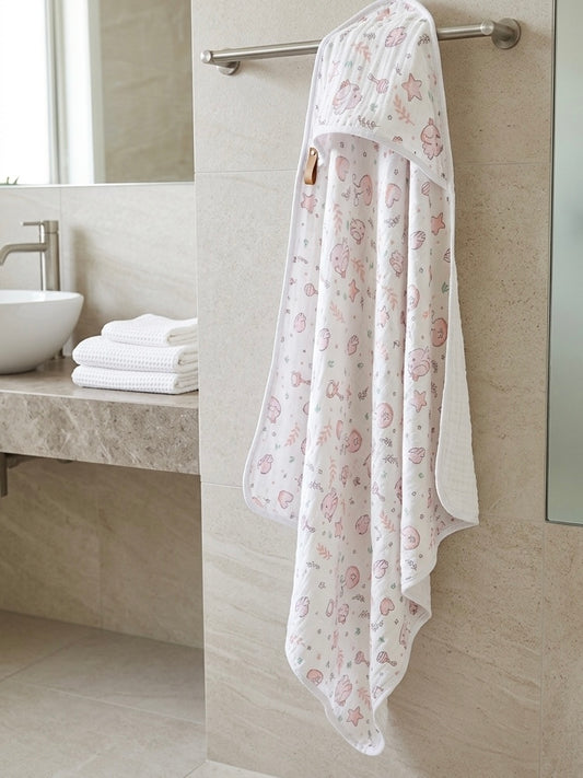 A hooded towel baby wrap or blanket with a pink teddy bear pattern hanging from a metal towel bar on a beige tiled bathroom wall.