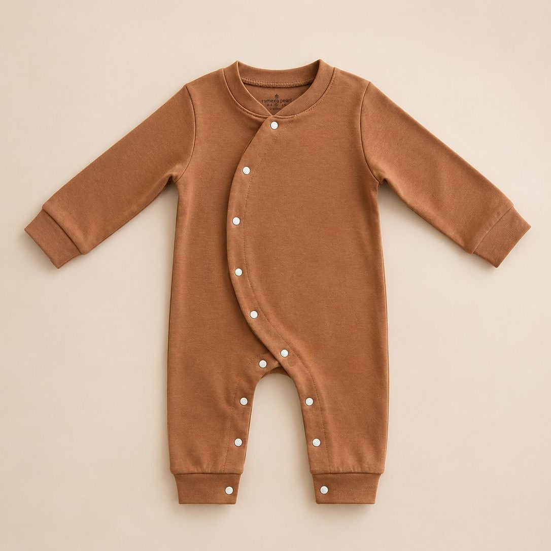 A long-sleeve baby romper in a warm camel brown color, featuring a snap-button closure down the front and on the legs, laid flat on a light beige background.