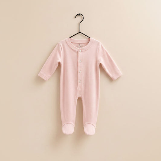 A light pink long-sleeve baby footed romper with a buttoned henley neckline, hanging on a wooden hanger against a solid beige background.