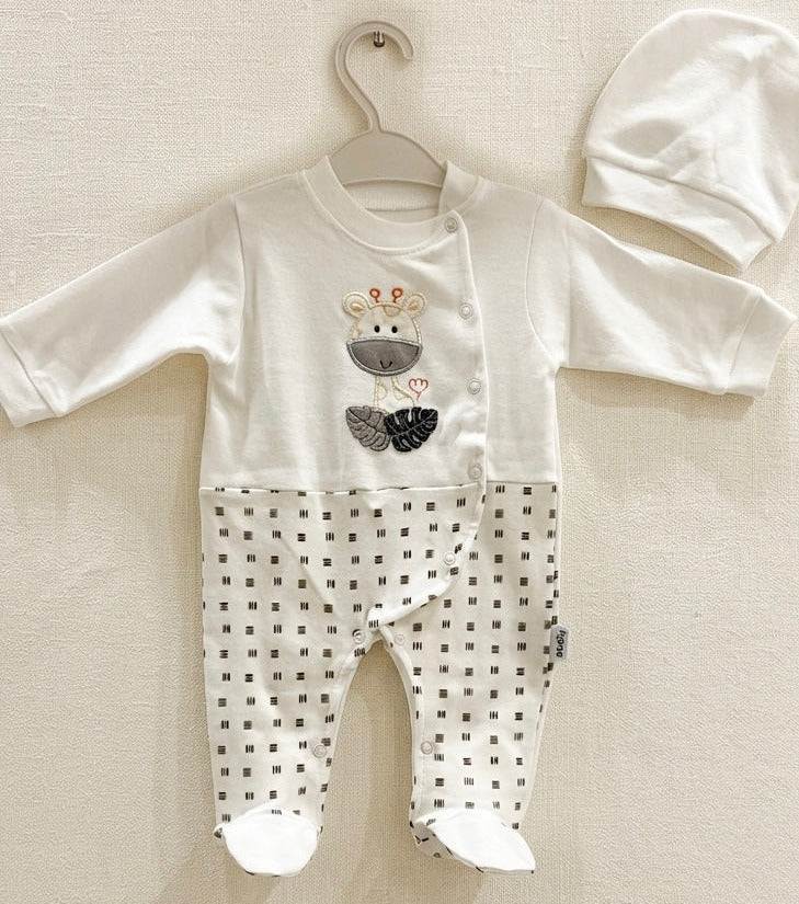 A baby footed sleeper set consisting of a white long-sleeve romper with a bear graphic on the chest and black polka dot patterned legs, shown hanging on a white hanger next to a matching white bonnet.
