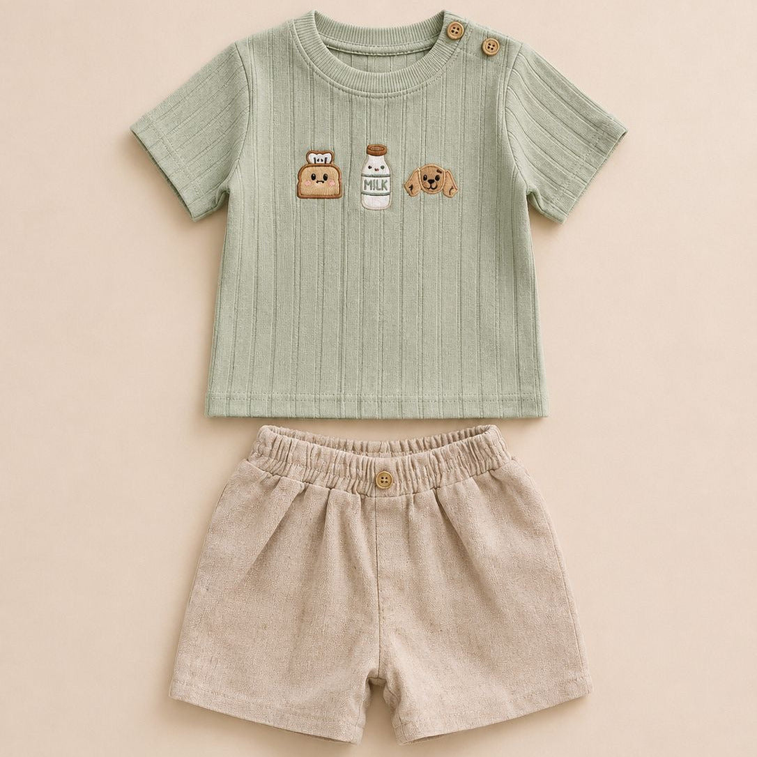 A baby two-piece outfit set featuring a light sage green ribbed short-sleeve top with cute cartoon graphics on the chest and beige linen shorts with an elastic waistband, laid flat on a warm beige background.