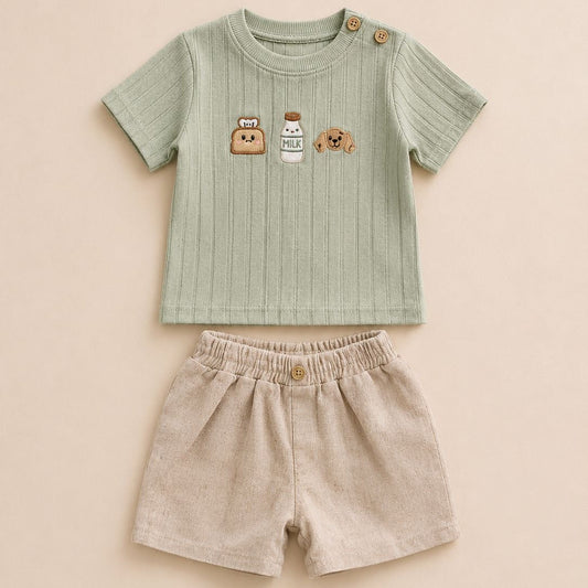 A baby two-piece outfit set featuring a light sage green ribbed short-sleeve top with cute cartoon graphics on the chest and beige linen shorts with an elastic waistband, laid flat on a warm beige background.