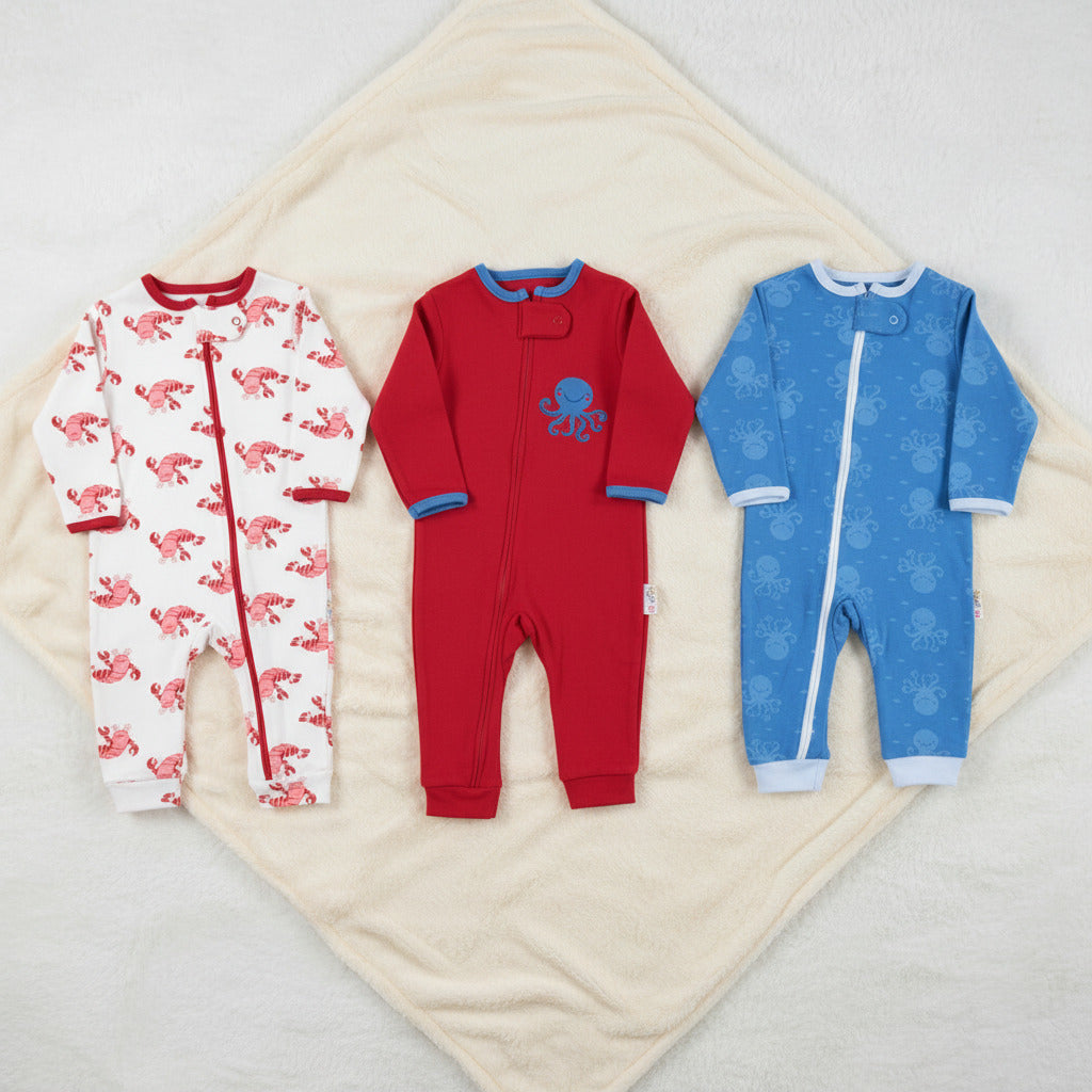 Three baby long-sleeve footless one-piece sleepers shown side by side on a white background: a white sleeper with pink flamingo print, a red sleeper with blue trim and a blue octopus graphic, and a blue sleeper with a subtle blue pattern.