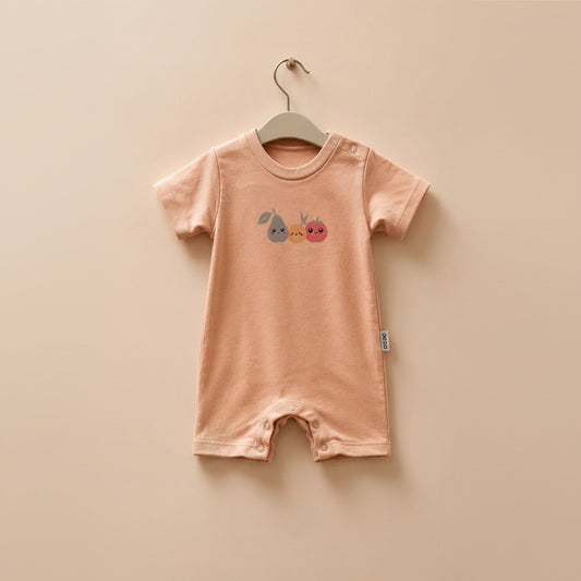 A baby short-sleeve romper in a soft peach-pink color, hanging on a wooden hanger against a matching light beige background. The romper features a small graphic of a blue pear, a yellow bunny, and a red strawberry on the chest.