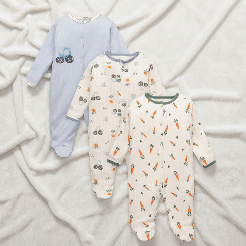 Three baby footed sleepers laid out on a light background. The left sleeper is light blue with a tractor graphic.