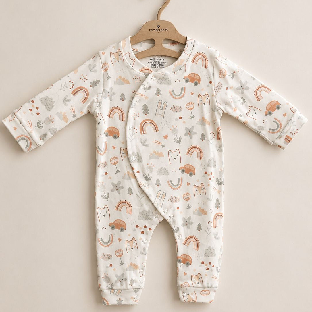 A baby long-sleeve footless romper with an all-over woodland print of rainbows, trees, and animals, hanging on a wooden hanger against a solid beige background.
