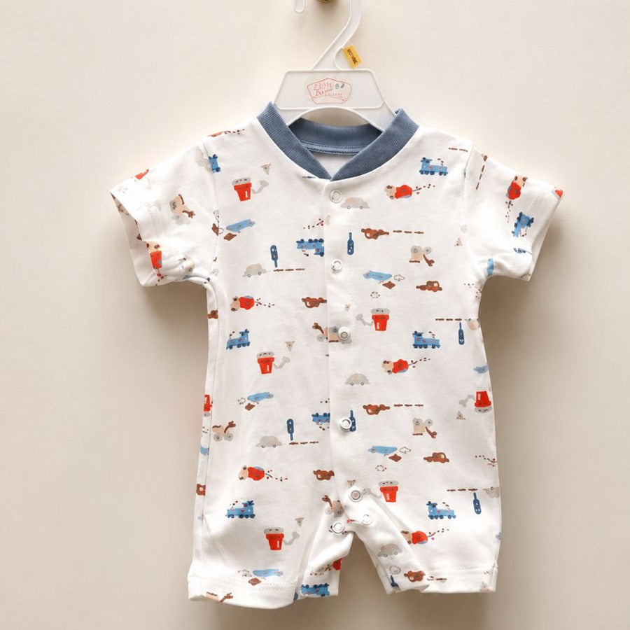 A baby short-sleeve romper hanging on a white plastic hanger against a plain beige wall. The romper is white with a blue collar and an all-over print of small red, blue, and brown vehicles and figures.