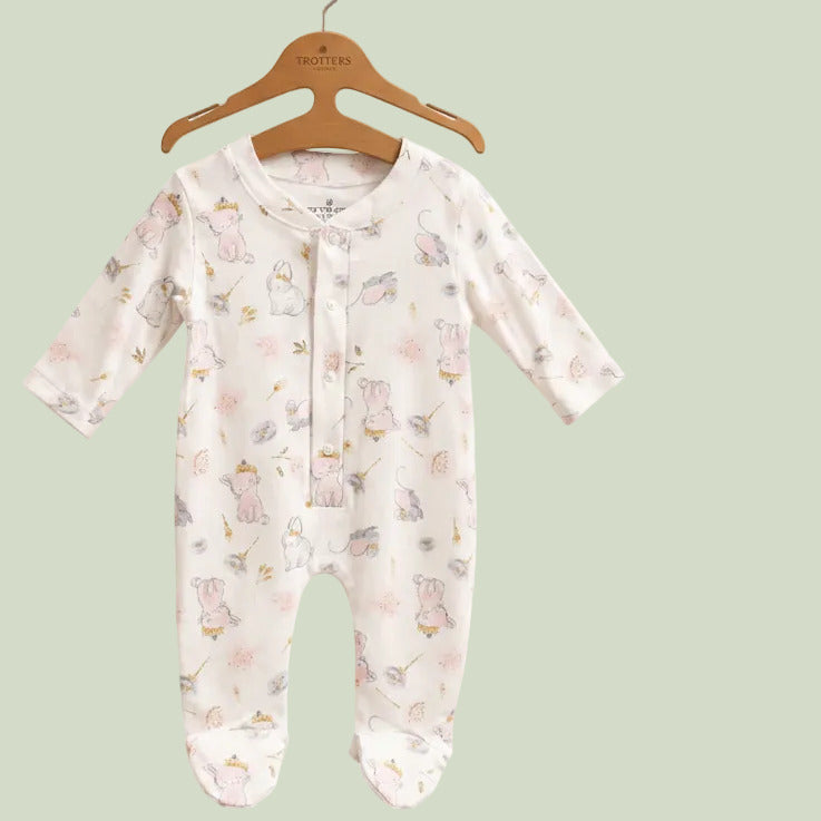 A baby long-sleeve footed sleeper in white with a delicate pink, yellow, and blue bunny print, hanging on a wooden hanger against a solid beige background.