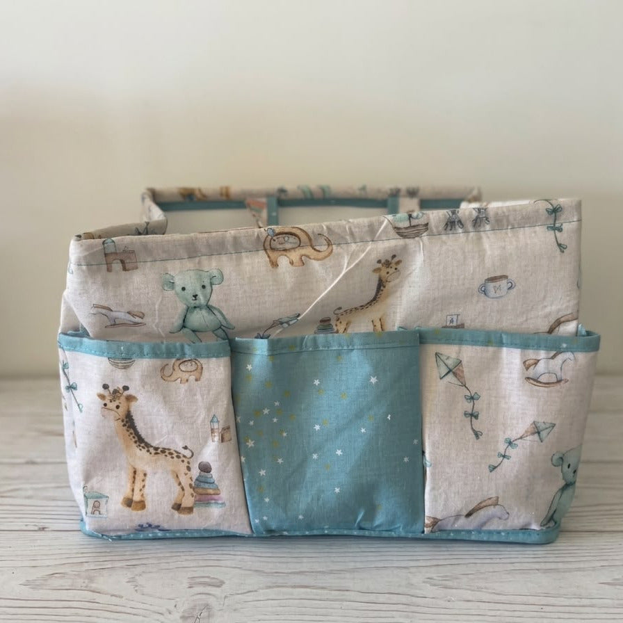 A fabric storage organizer basket with three front pockets, featuring a woodland safari animal print in beige and teal on a light wood surface.