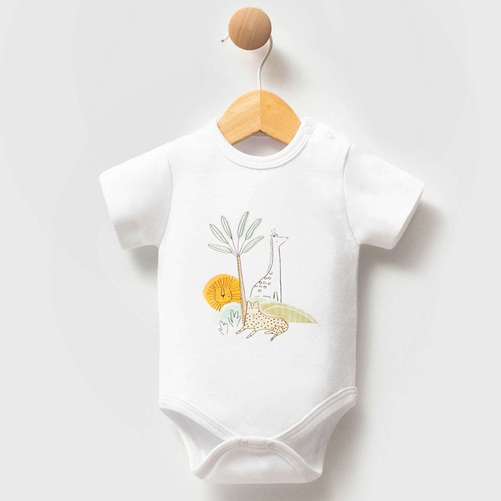 A white short-sleeve baby bodysuit hanging on a wooden hanger with a round wooden hook. The bodysuit features a colorful safari-themed graphic on the chest with a giraffe, lion, elephant, and palm tree.