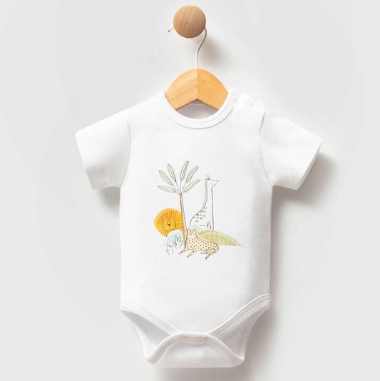 A white short-sleeve baby bodysuit hanging on a wooden hanger with a round wooden hook. The bodysuit features a colorful safari-themed graphic on the chest with a giraffe, lion, elephant, and palm tree.